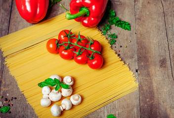 Italian dry pasta spaghetti with tomatoes and fresh herbs on a dark wooden background, selective focus