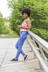 portrait of  a Happy young beautiful afro american woman smiling and using mobile phone. Green background. Spring or summer season. Casual