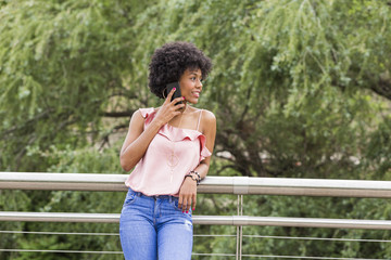 Naklejka premium portrait of a Happy young beautiful afro american woman smiling and talking on her mobile phone. Green background. Spring or summer season. Casual