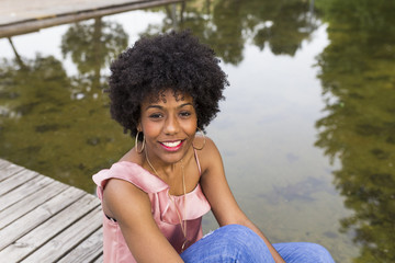 portrait of  a Happy young beautiful afro american woman sitting on wood floor and smiling. water background. Spring or summer season. Casual