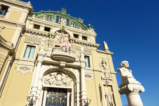 Monte-Carlo Opera House and casino west entrance in Monaco with statue of composer Jules Massenet on blue sky day
