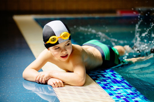 Sporty cute little boy lying on the stomach by the edge of swimming pool and splashing