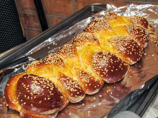 Fresh homemade large loaf of yellow Challah bread on aluminum foil from oven sprinkled with sesame...