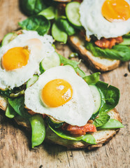 Healthy breakfast sandwiches. Bread toasts with fried eggs and fresh vegetables on rustic wooden board background, selective focus. Clean eating, healthy, diet, weight loss, detox food concept