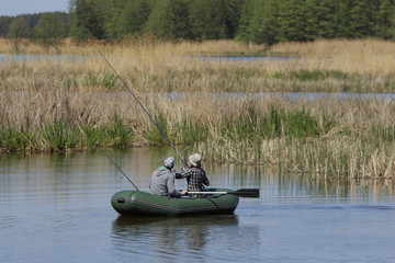 Fototapeta na wymiar Family of unidefied man and woman fishing in inflatable boat at the river with a lot of bulrush