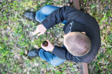 A sitting man with a short haircut with a bottle and a cigarette in his hands. Blurry. View from above