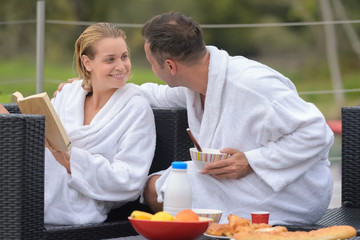 couple on white bathrobe having breakfast outdoors