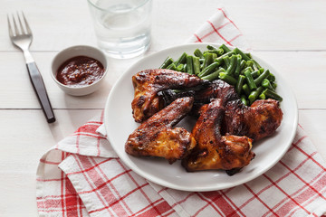 Grilled chicken wings with green beans on a white plate
