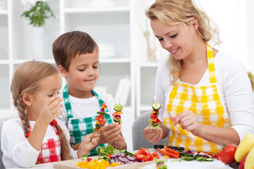 Young kids with their mother in the kitchen - preparing a vegetables snack