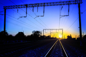 Fototapeta na wymiar Railway - Railroad at sunset with sun, Rails and electric lines in yellow light