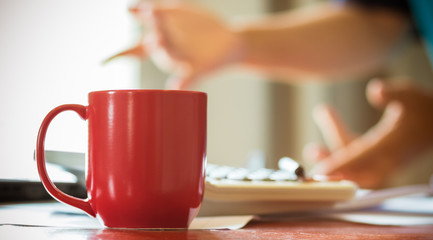 View of red coffee cup with blur hand gestures, hands of successful businessmen with confident businessman sitting at meeting room for discussion, selective focus