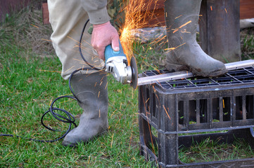 The process of cutting and polishing metal products at home. A man with an electric saw and sparks.