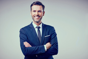 Portrait of handsome man standing with crossed arms, wearing suit smiling. Isolated