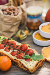 Pie with cherry tomatoes, pumpkin pie, orange and paper bag with nuts on a wooden table