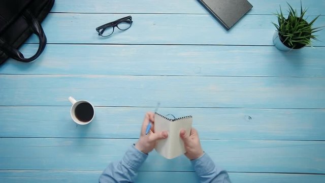 Top view male hands writing in notebook on white desk from above