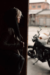 Fototapeta na wymiar A young woman with a leather bag near the garage. A woman in a leather jacket. Motorcycle near the garage. Leather bag