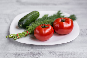 Fresh dill, cucumber and tomato on a table in a plate. Ecological wooden background.