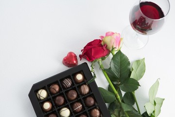Chocolate box, roses and red wine glass on white background
