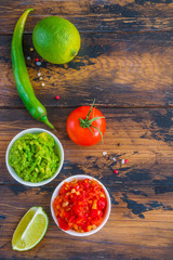 Homemade salsa and guacamole sauces in small white bowls on the wooden rustic table, top view.