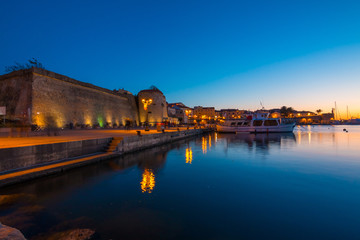 Naklejka premium Alghero cityscape seen from the harbor at night, Italy