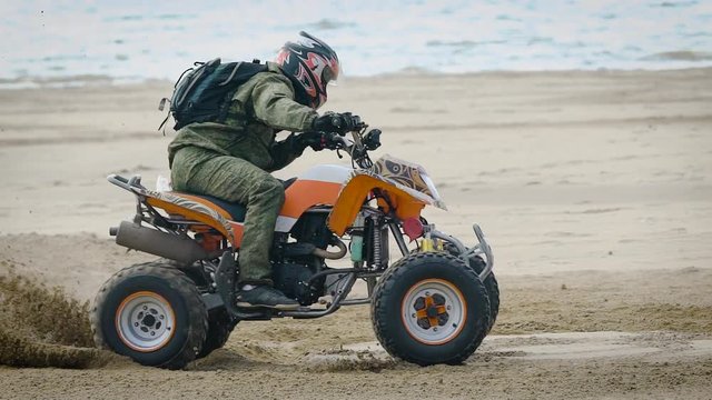 An adult man performs a trick on a sports quad bike riding on a sandy beach, a person professionally manages an extreme country of transport