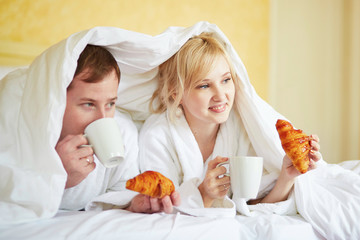Couple in white bathrobes having breakfast in bed