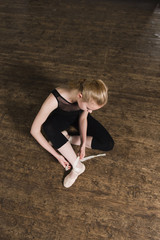 Young ballerina or dancer girl putting on her ballet shoes on the wooden floor. Female dancer ties on her pink ballet slippers with ribbons. Top view. © o_lypa