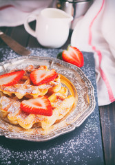 Homemade classic Belgian waffles topped with fresh strawberry and powdered sugar on vintage plate