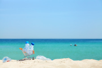 Miniature shopping cart with empty plastic bottles left by tourist on a tropical beach, environmental pollution concept picture, selective focus.