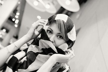 Junge Frau beim Shopping in einem Modehaus, verhüllt ihr Gesicht mit einem Tuch