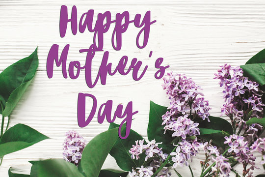 happy mother's day text sign. greeting card. gentle pink lilac flowers on white rustic wooden background. tender soft image. mothers day concept. flat lay