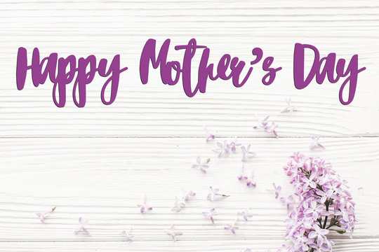 happy mother's day text sign. greeting card. gentle pink lilac flowers on white rustic wooden background. tender soft image. mothers day concept. flat lay