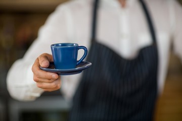 Mid-section of waiter offering a cup of coffee