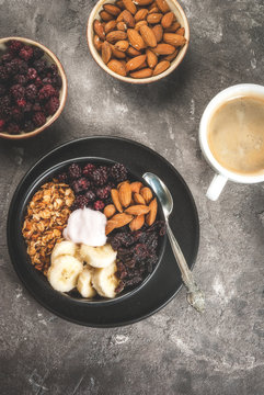 Buddha bowl. Concept of healthy balanced diet breakfast: oatmeal granola, dried cherries, blackberries, banana, nuts almonds and yogurt. On a gray stone table, with cup of coffee top view copy space