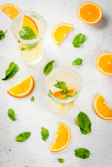 Summer drink. Fresh orange and mint lemonade with ice in glasses, light grey stone marble table, selective focus