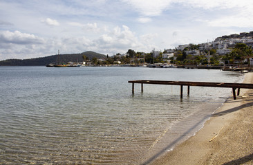 View of a small pier in bay at Turkbuku village in autumn. Summer houses and cloudy sky are in the background. Town is in Bodrum peninsula located in southwestern Turkey.