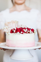 Woman holding sweet white cream mousse cake with raspberries on cake stand
