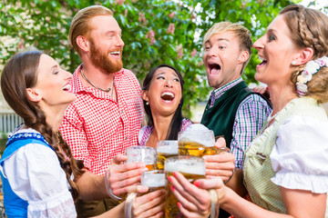 Fünf Freunde, Männer und Frauen, haben Spass in Biergarten beim Anstoßen mit Maßkrügen