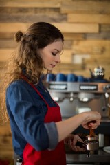 Waitress using a tamper to press ground coffee