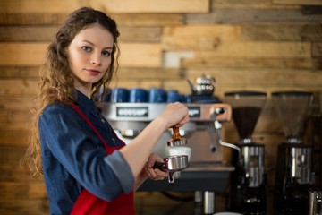 Fototapeta na wymiar Waitress using a tamper to press ground coffee 