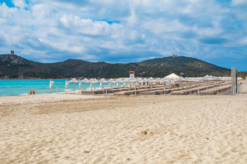Fototapeta na wymiar Sunbeds with umbrellas on white sand beach in Villasimius beach, Sardinia island, Italy