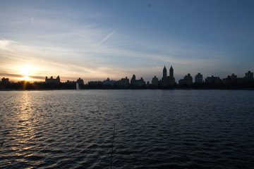 Sunset reflects on lake and silhouette buildings with blue sky