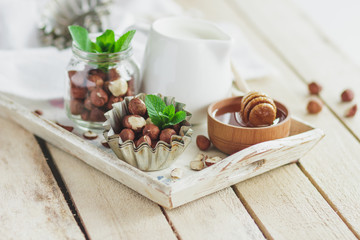 Honey in the wooden bowl, mint leaves, hazelnuts and jar with milk on the wooden tray