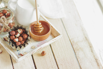 Honey in the wooden bowl, hazelnuts and jar with milk on the wooden tray