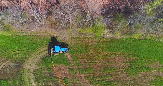 Tractor fertilizing field with liquid manure pumped from distant tanker truck via giant hose, aerial view.