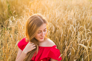 Portrait of a young woman in red dress on a background of golden oats field, summer outdoors.