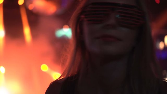 Closeup face of pretty smiling woman in pink leg glasses dancing at the party over disco lights background