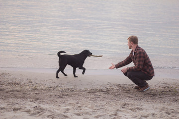 man with stick playing with black dog on the beach
