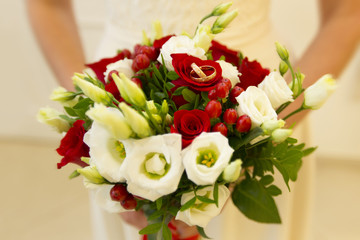 Золотые обручальные кольца с бриллиантами на свадебном букете из красных и белых роз с красными декоративными ягодами и красной лентой на столе из малахита. 