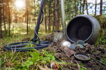 Metal detector, shovel, pot of treasure coins on the background of a sunny pine forest